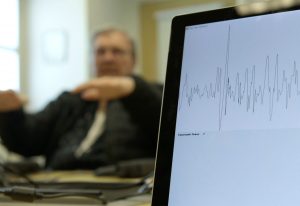 Close up of laptop screen with diagonostics. Man holding hands up in background