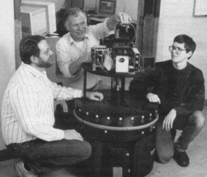 Three men squatting around a mobile robot