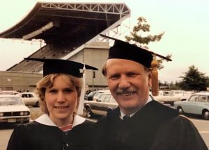 Two people standing next to each other in graduation caps in front of a stadium