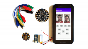 Photo of an Android smartphone, an Arduino microcontroller board, a Bluetooth Low Energy shield, alligator clips, a battery and a charger.