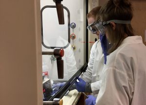 Two people in lab coats work on a project in front of a lab window