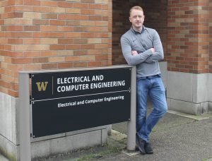 Cody Brereton standing next to the UW ECE sign outside the Paul Allen Center