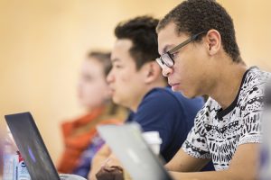 Three students sitting at a desk and working on laptops