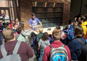 A man demonstrates a device in front of a group of K–12 students