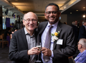 Rico Malvar and Radha Poovendran toasting with champagne glasses and smiling for the camera