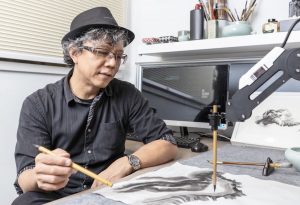 Victor Wong sitting at a desk with a paintbrush, next to an A.I. calligraphy arm