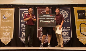 Three men standing on stage with the center one holding a sign. 