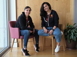 Iliana Montauk and Laila Abudahi sitting in chairs next to each other and smiling at the camera