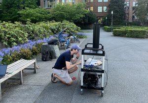 Two students using scientific equipment in front of Drumheller Fountain on the UW campus