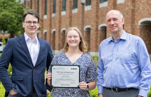 Margot Adam holding a certificate and standing in between UW ECE Chair Eric Klavins on her left and UW ECE Professor Daniel Kirschen on her right. The photo was taken outside of the UW ECE building on a summer day.