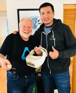 UW Professor Emeritus Tom Furness is holding a virtual reality headset and standing next to Alvin Graylin in front of the HIT Lab