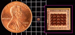 A close up of a penny on a black-and-white grid. To the right of the penny is a tiny microchip, about 1/20th the size of the penny.