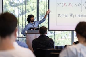 Aaditya Ramdas, a professor from Carnegie Mellon University, standing in front of a screen, at a podium, giving a talk at the workshop.