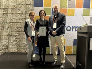 UW ECE Maryam Fazel stands on a stage, holding an award certificate. The award presenters stand on either side of her.