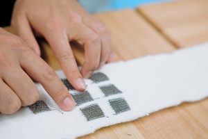 A closeup of MultiSensKnit, showing two hands pointing to gray squares on the white fabric.