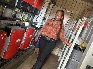Eliane Nirere in a small room, standing next to a rack of large power batteries