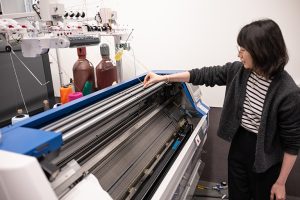 UW ECE Assistant Professor Yiyue Luo standing next to and adjusting a digital knitting machine