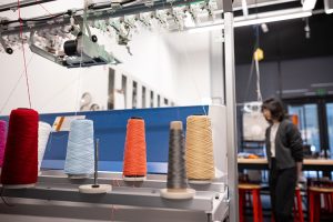 A closeup of colorful spools atop the digital knitting machine. UW ECE Assistant Professor Yiyue Luo is in the background of the photo.