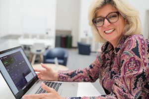 PMP student Bita Massoudi smiling and sitting at a table in front of a laptop.