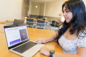 Devika Nair sitting at a table with her laptop in front of her. The RespiraEdge app is on the screen.